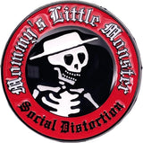 A circular novelty pin or badge featuring a black center with a white skull wearing a white hat, surrounded by a red outer ring with gothic white text reading 'Baby's Little Monster' and 'Social Distortion'.