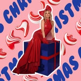 Woman in a red dress sitting on a blue gift box with Christmas-themed background