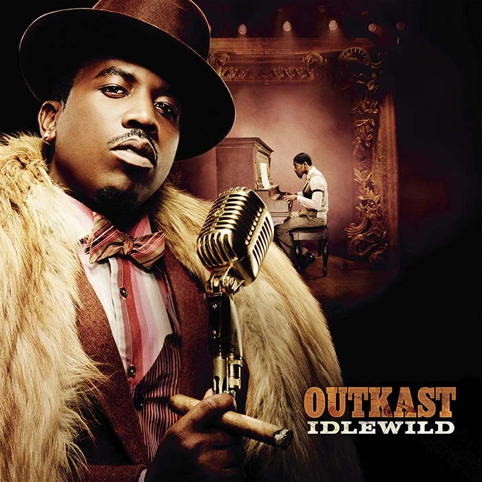 Album cover art for Outkast's 'Idlewild', featuring a close-up portrait of a man in a brown fedora and fur coat holding a vintage microphone, with a smaller scene of a pianist in the background.