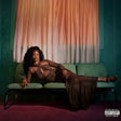 Person in a leopard print outfit sitting on a green couch with aParental Advisory label.