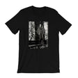 A black short-sleeve crewneck t-shirt featuring a rectangular black-and-white graphic print on the front, depicting a figure in a trench coat standing in front of a brick wall.