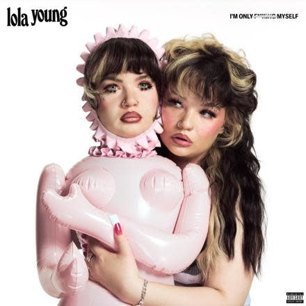Two individuals with styled hair holding a pink inflatable object, with 'lola young' branding.