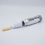 A pump-action marker pen shown open with the cap removed, revealing the internal plunger and a small beige felt tip. The barrel is white with black printed branding and text, photographed on a clean light gray background.