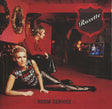 Roxette's 'Room Service' album cover, featuring two women in a red-lit room. One woman in a patterned top and black leather pants reclines on the red carpet in the foreground, while another woman in a red top and black leather pants sits behind her.