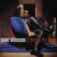 Album cover featuring a person in a black leather outfit sitting on a blue chair, holding a microphone.