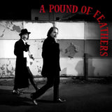 Two men in formal attire walking past a wall with 'A Pound of Feathers' text.