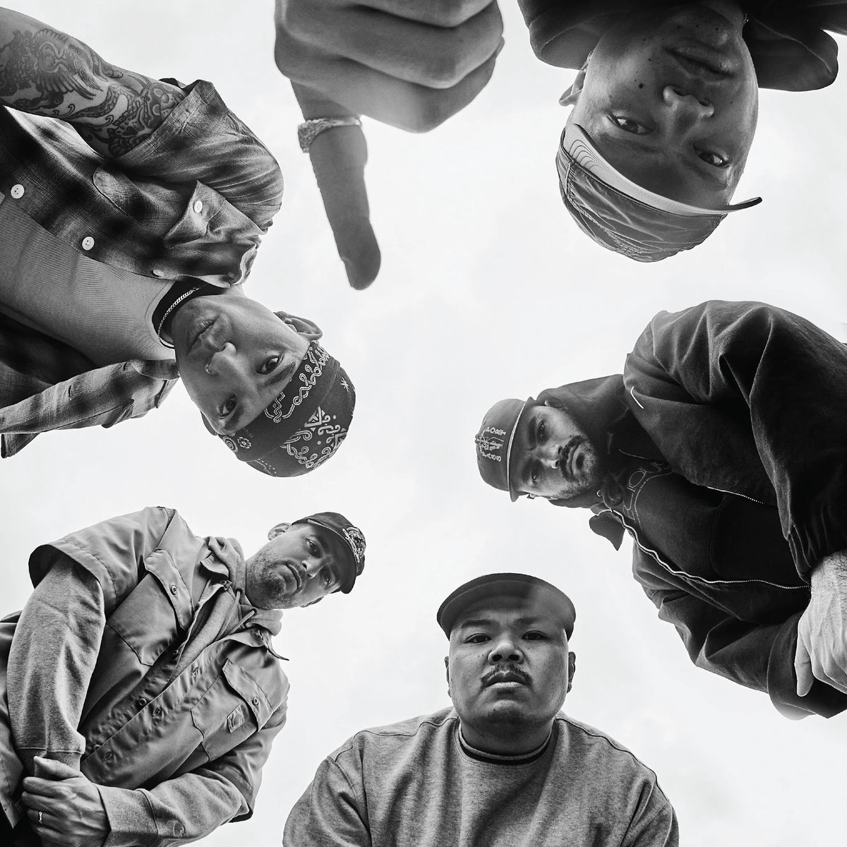 Black and white photo of six people standing in a circle with a neutral background