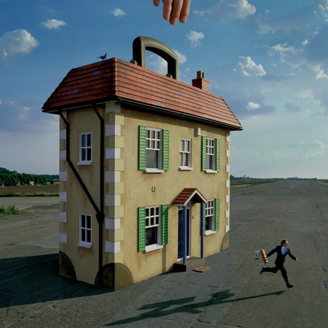 House-shaped suitcase with a person running away on a road under a blue sky.