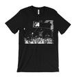 A black short-sleeve crewneck t-shirt featuring a black and white graphic print of a crowd in front of a building with a '50' sign, displayed on a solid white background.