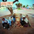 The image shows the members of Jurassic 5 sitting around a large tree stump with the album 'Quality Control' written above. They are dressed in casual clothing and the setting appears to be an outdoor location, possibly a street or park.